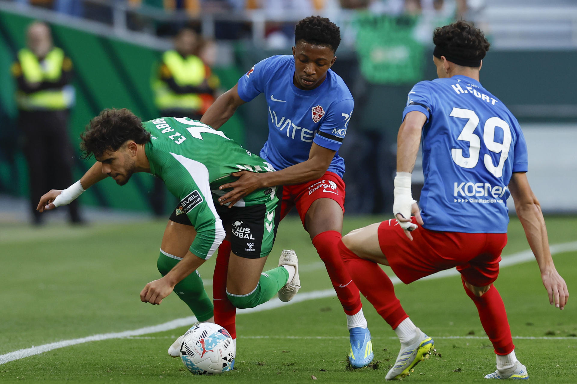 El delantero del Betis Abde Ezzalzouli (i) trata de escapar de Buba Sangaré (c), del Elche, durante el partido de LaLiga de fútbol que Real Betis y Elche CF disputan en el estadio de La Cartuja. EFE/Julio Muñoz
