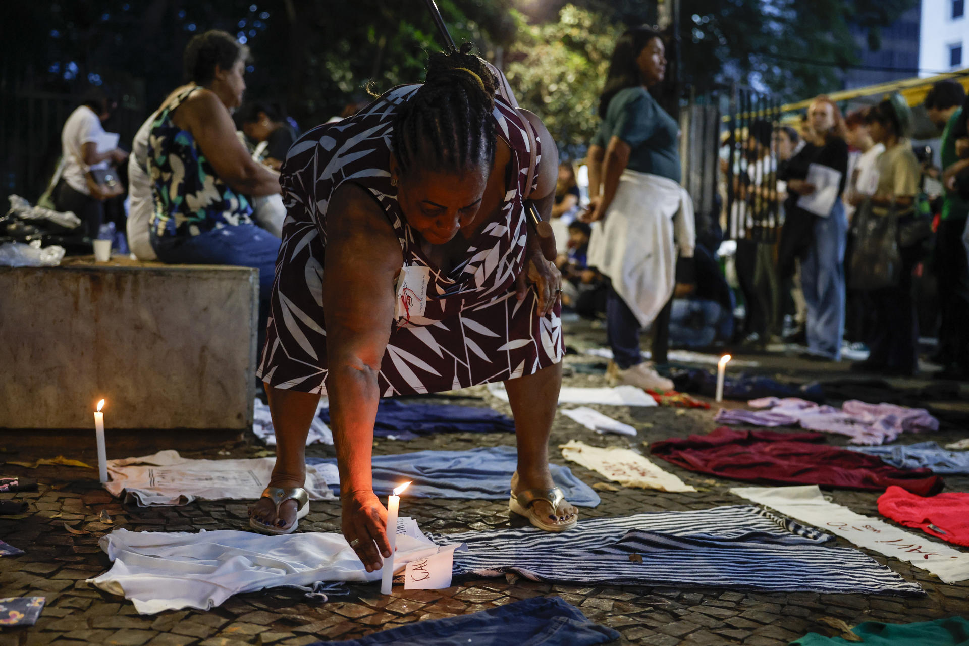 Una integrante del movimiento Madres de Mayo coloca una vela junto a algunas prendas durante una manifestación este sábado, en Sao Paulo (Brasil). EFE/ Sebastiao Moreira
