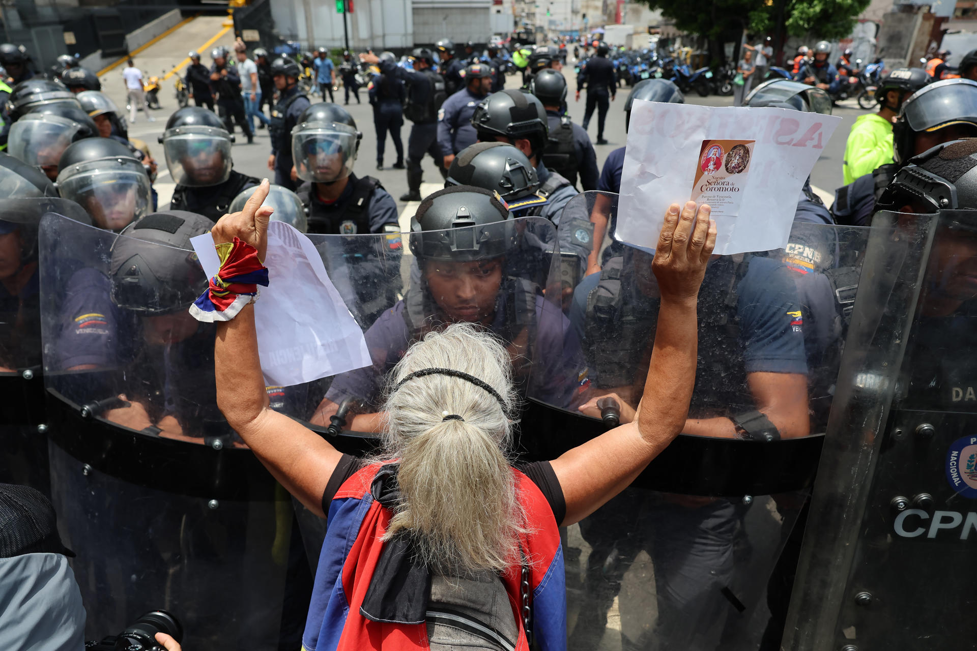 Una persona muestra carteles a integrantes del Cuerpo de Policía Nacional Bolivariana (CPNB) este lunes, durante un homenaje por la muerte de Carmen Navas, en Caracas (Venezuela). EFE/ Miguel Gutiérrez
