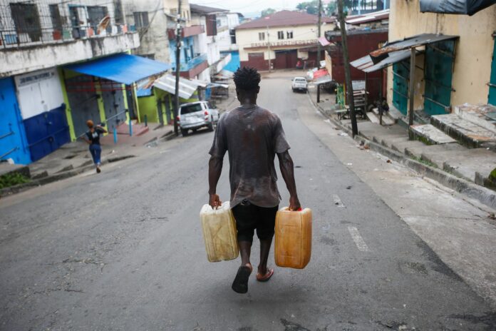 Un hombre camina con unos bidones de agua en Monrovia, Liberia. EFE/EPA/AHMED JALLANZO
