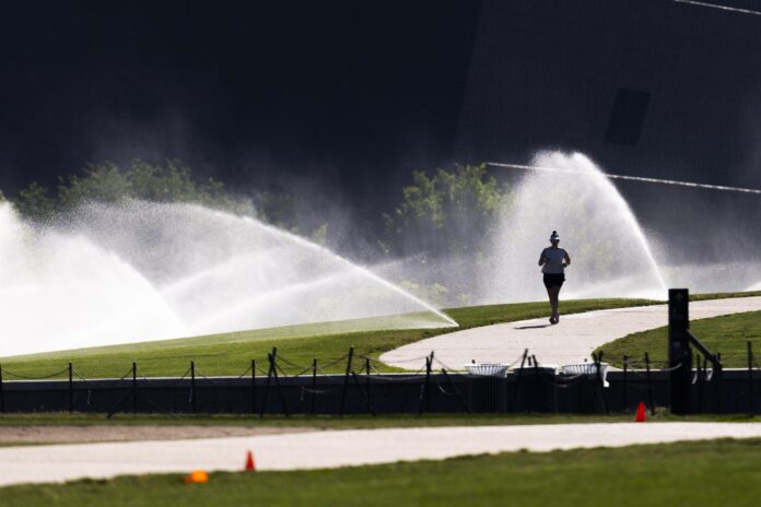 Un corredor pasa junto a unos aspersores en el National Mall, frente al National Museum of African American History and Culture, también conocido como el Blacksonian, en Washington, DC, EE.UU. EFE/JIM LO SCALZO
