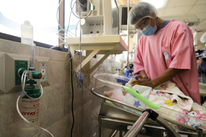 Un integrante del personal hospitalario da de comer a un bebé conectado a una cánula de oxígeno este jueves, en un hospital en La Paz (Bolivia). EFE/ Gabriel Márquez
