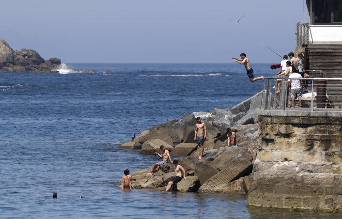 Bañistas disfrutan de un dia veraniego en el puerto pesquero de San Sebastián. EFE/Juan Herrero
