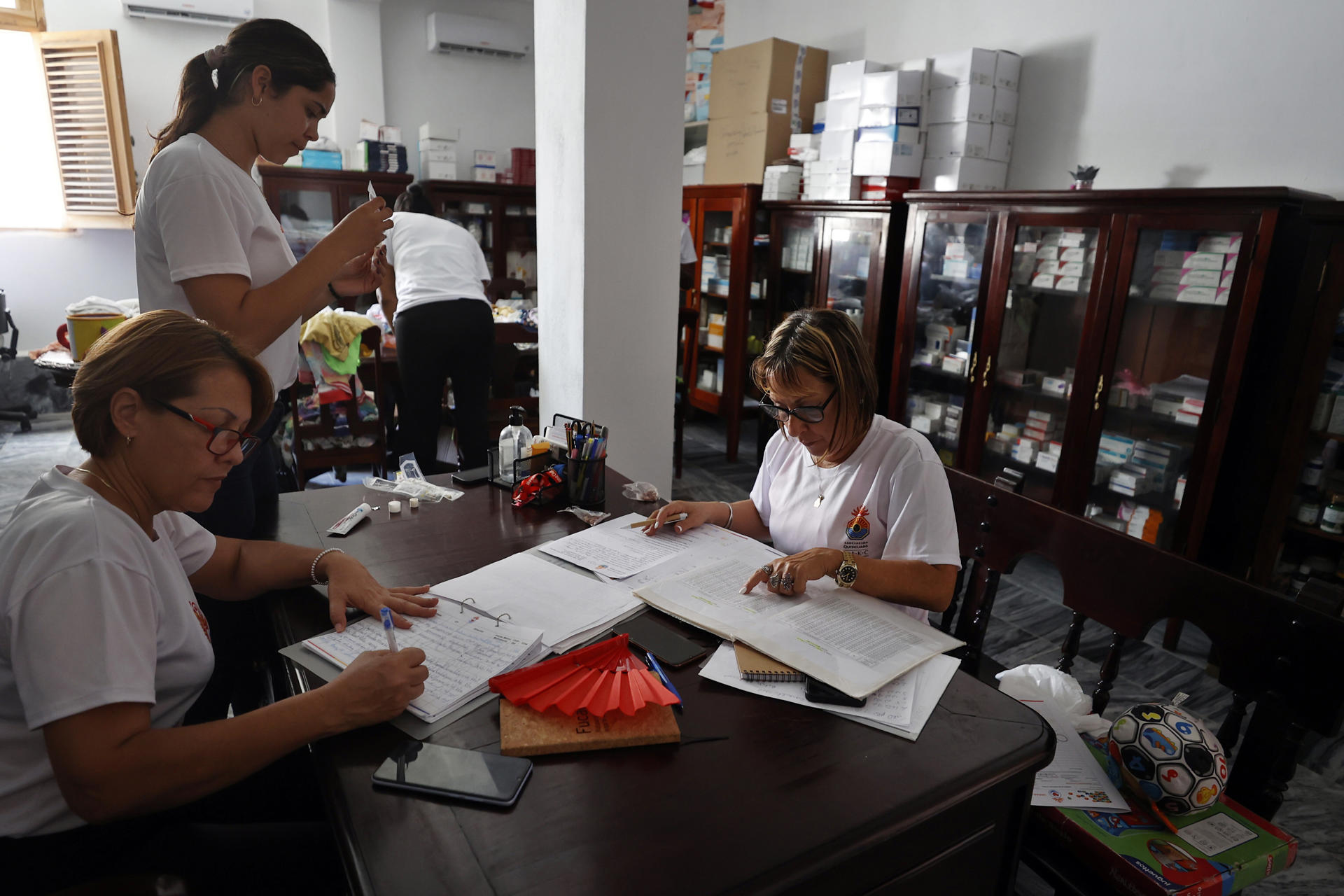 Personas trabajan en la farmacia de la ONG Quisicuaba este lunes, en La Habana (Cuba). Delgadísimos y agotados, los ancianos esperan pacientemente a escuchar su número para recoger un pozuelo de comida caliente de la cocina social de la mayor ONG de Cuba. Son más de un centenar y no paran de llegar más. EFE/ Ernesto Mastrascusa
