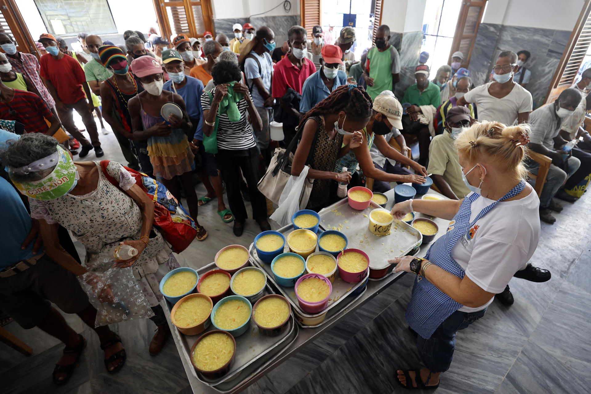 Personas reciben alimentos por personal de la ONG Quisicuaba este lunes, en La Habana (Cuba). Delgadísimos y agotados, los ancianos esperan pacientemente a escuchar su número para recoger un pozuelo de comida caliente de la cocina social de la mayor ONG de Cuba. Son más de un centenar y no paran de llegar más. EFE/ Ernesto Mastrascusa
