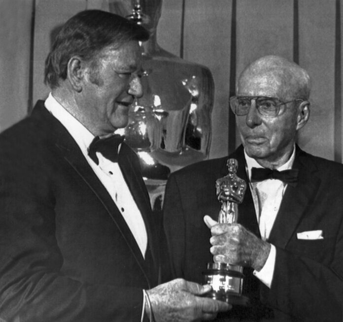 El actor John Wayne (i) entrega el Oscar honorífico, por su contribución al arte cinematográfico, al director y productor estadouniense Howard Hawks, que nació un día como hoy de hace 130 años. EFE/UPI/rsa/Archivo
