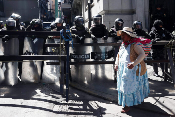Una mujer aimara camina frente a un grupo de policías durante una protesta que exige la renuncia del presidente de Bolivia, Rodrigo Paz, por quinta semana consecutiva este lunes, en La Paz (Bolivia). EFE/Luis Gandarillas
