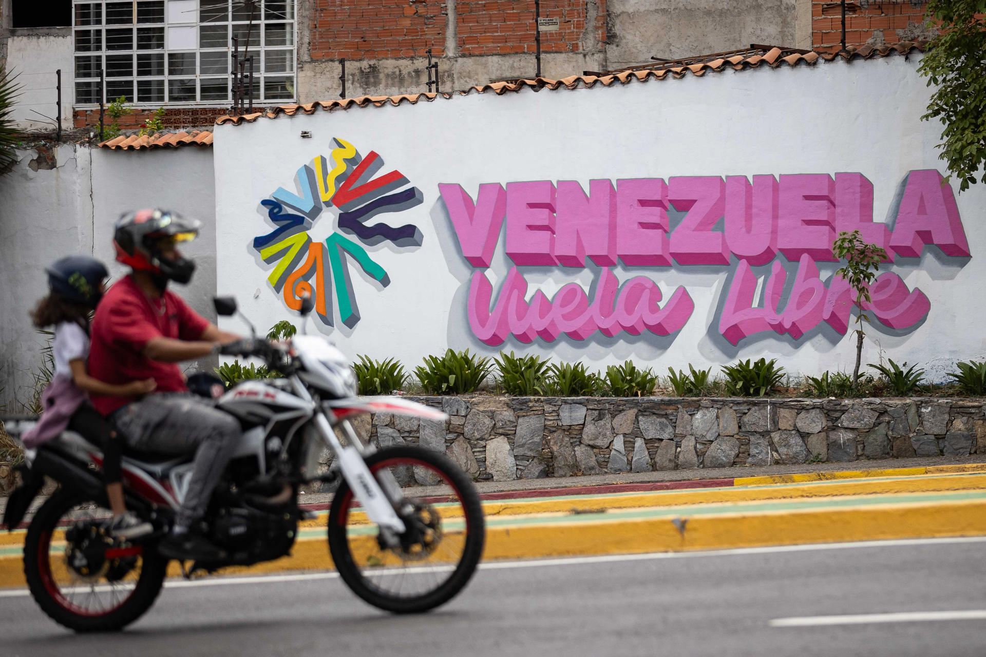 Fotografía del 31 de mayo del 2026 que muestra a personas transitando en motocicleta frente a un mural de Venezuela Libre, en Caracas (Venezuela). EFE/ Ronald Peña R
