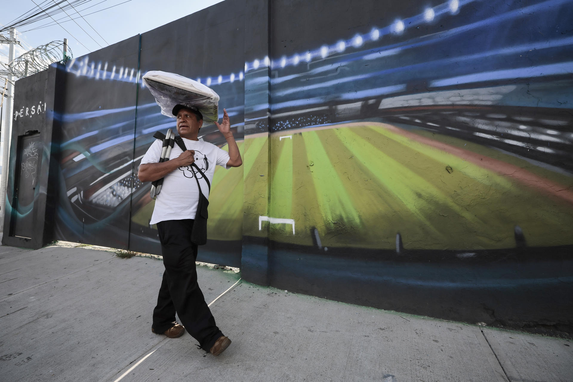 Un vendedor camina frente a un mural que adorna una casa cercana al estadio Ciudad de México este miércoles, en Ciudad de México (México). EFE/ José Méndez
