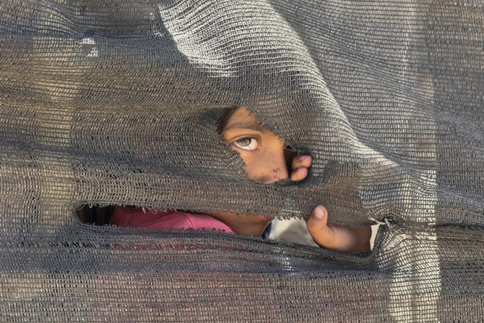 Una niña se asoma tras una tienda improvisada en el puerto en la Ciudad de Gaza, donde miles de personas desplazadas por los ataques israelíes han encontrado refugio, en mayo de 2025. EFE/ Ahmad Awad
