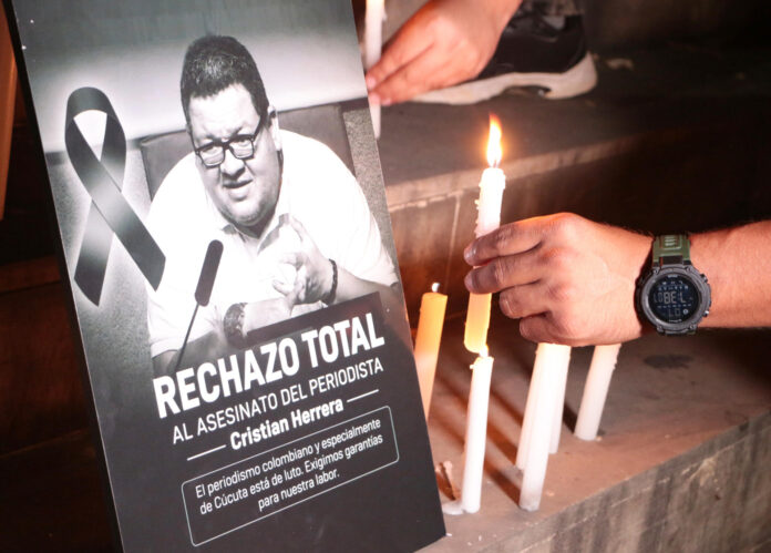 Detalle de las manos de dos personas al poner un par de velas junto al retrato del periodista colombiano Cristian Herrera, asesinado este 6 de junio, en Cúcuta (Colombia).  EFE/Mario Caicedo
