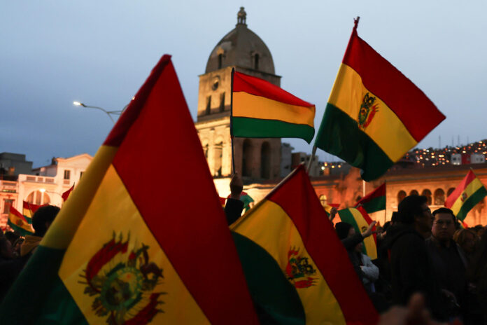 Personas ondean banderas durante un cabildo donde exigen al gobierno declarar estado de excepción este martes, en el atrio de la basílica de San Francisco en La Paz (Bolivia). EFE/ Luis Gandarillas
