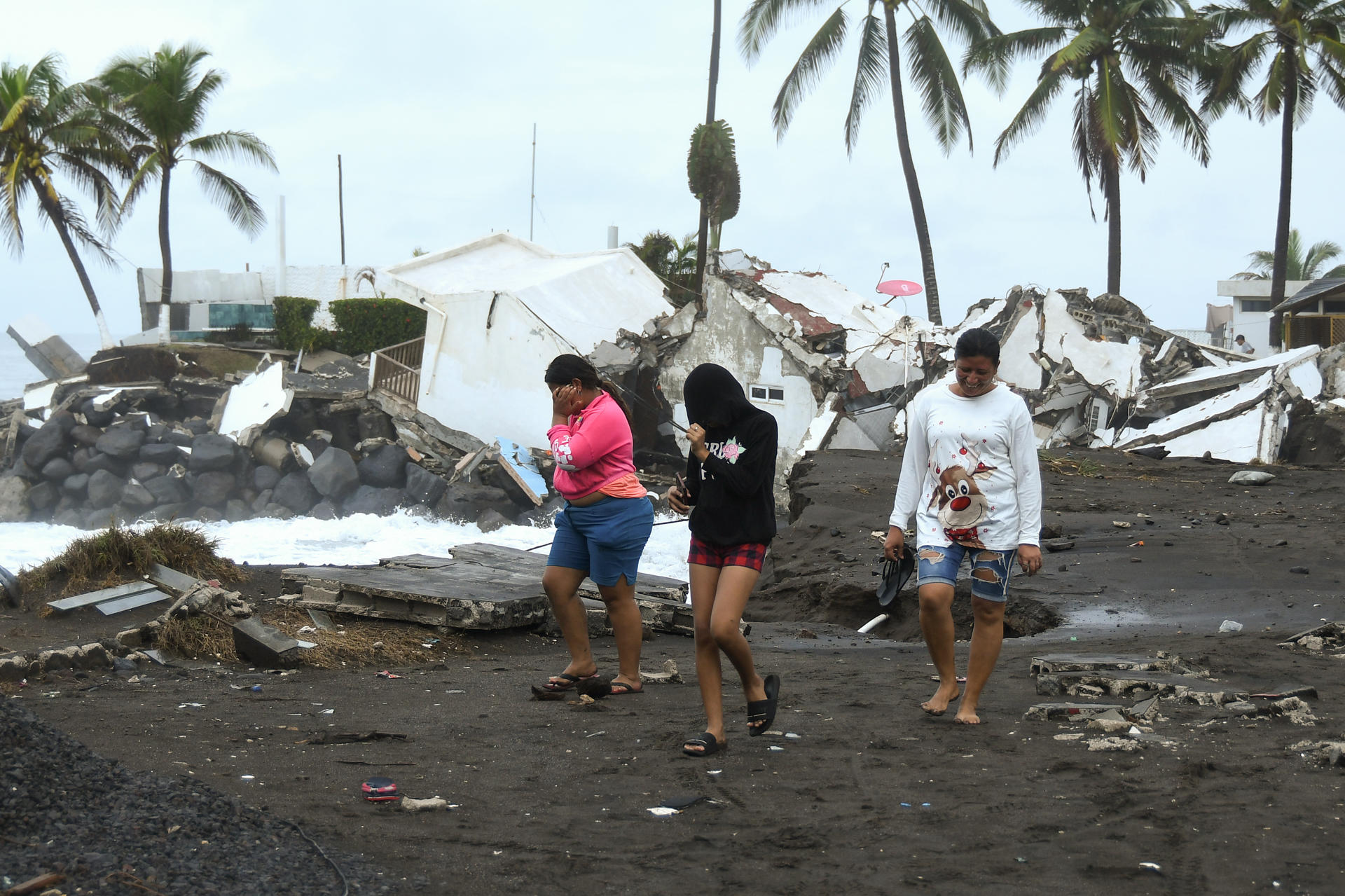 Personas caminan cerca de viviendas destruidas debido al fuerte oleaje y constantes lluvias generadas por la tormenta tropical Cristina este miércoles en el puerto de Iztapa (Guatemala). EFE/ Alex Cruz