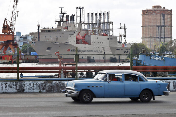 Fotografía de archivo en la que se captó el paso de un automóvil viejo frente a una planta generadora de electricidad en La Habana (Cuba). EFE/Ernesto Mastrascusa
