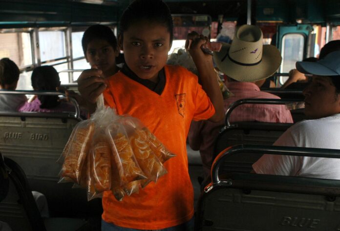 Fotografía de un niño al vender bolsas de mandarinas en un autobús en Tegucigalpa (Honduras). EFE/Gustavo Amador
