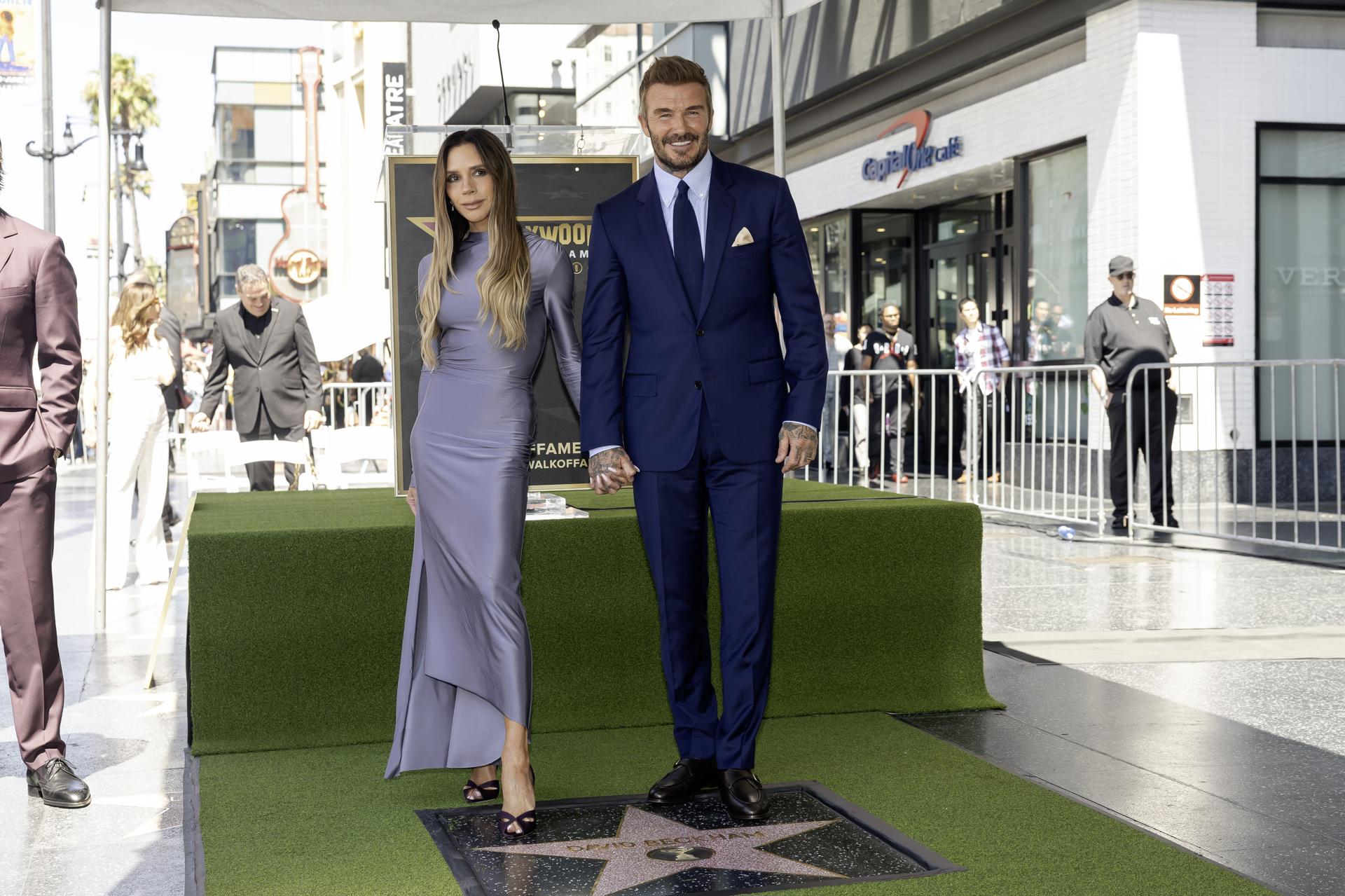 El exfutbolista británico David Beckham (c) fue captado, este 12 de junio, al posar junto a su esposa, la cantante Victoria Beckham (I), durante una ceremonia en la que fue distinguido con una estrella en el Paseo de la Fama de Hollywood, en Los Ángeles (CA, EE.UU.). EFE/Ted Soqui
