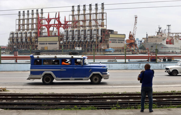 Fotografía de archivo en la que se captó un auto viejo de transporte colectivo al pasar frente a una planta flotante de generación eléctrica en el puerto de La Habana (Cuba). EFE/Ernesto Mastrascusa
