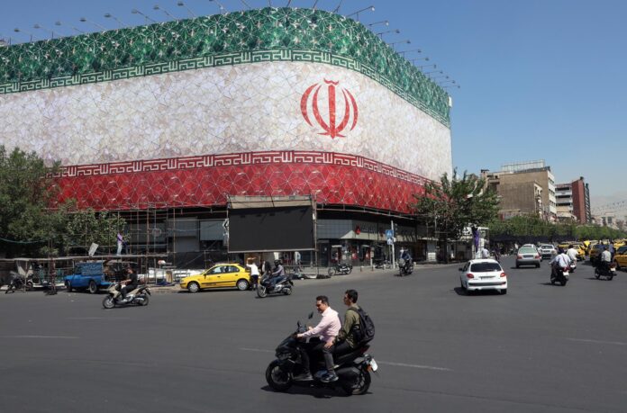 Unos iraníes pasan en coche junto a una valla publicitaria con la bandera nacional de Irán en la plaza Enqelab de Teherán, Irán. EFE/Abedin Taherkenareh
