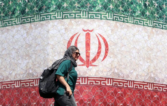 TEHERÁN (IRÁN), 14/06/2026.- Una mujer iraní pasa junto a una valla publicitaria con la bandera nacional de Irán en la plaza Enqelab de Teherán, Irán, este domingo.
 EFE/EPA/ABEDIN TAHERKENAREH
