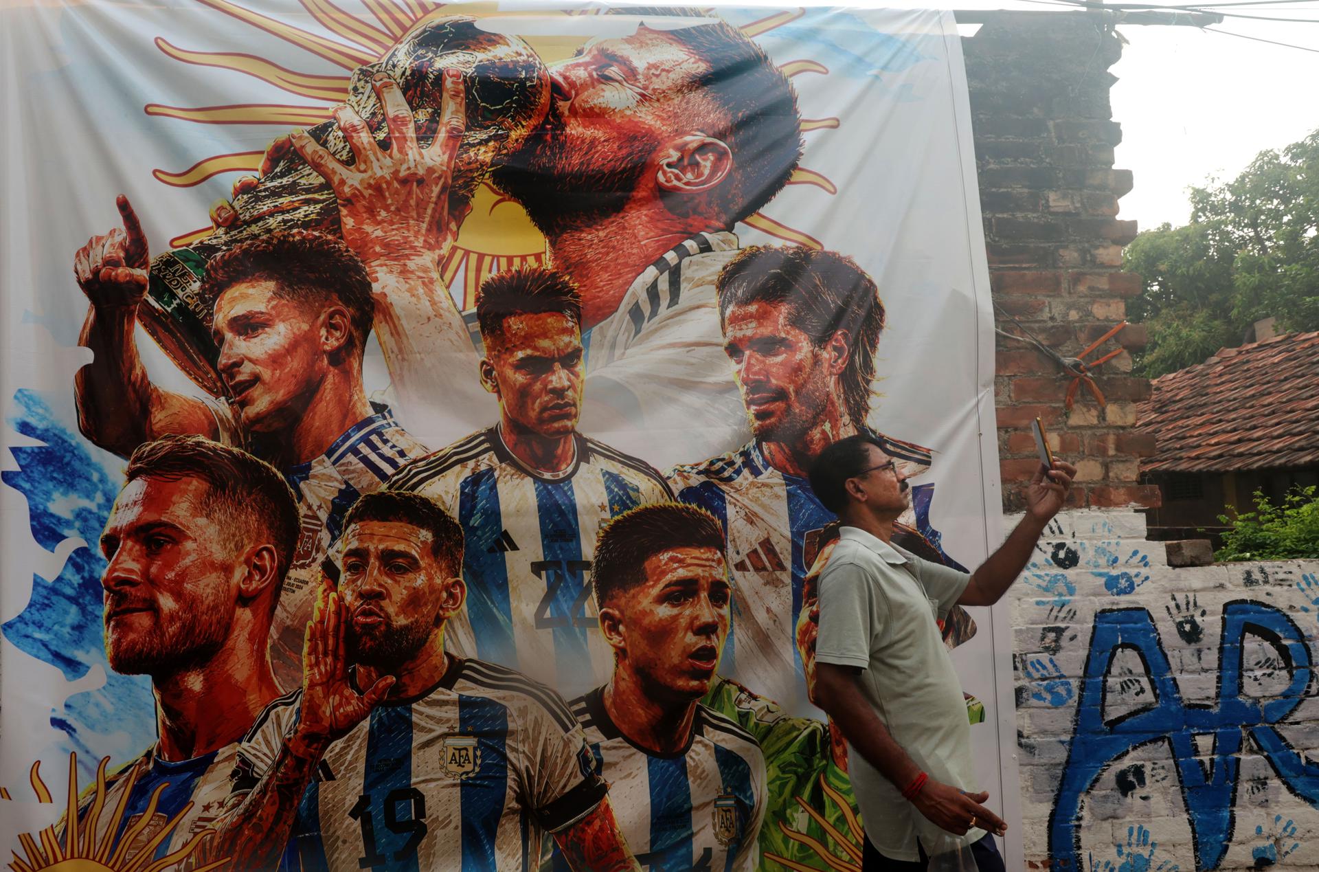 Un hombre se toma una fotografía junto a un muro con imágenes de futbolistas argentinos en Howrah (Calcuta, India). EFE/PIYAL ADHIKARY