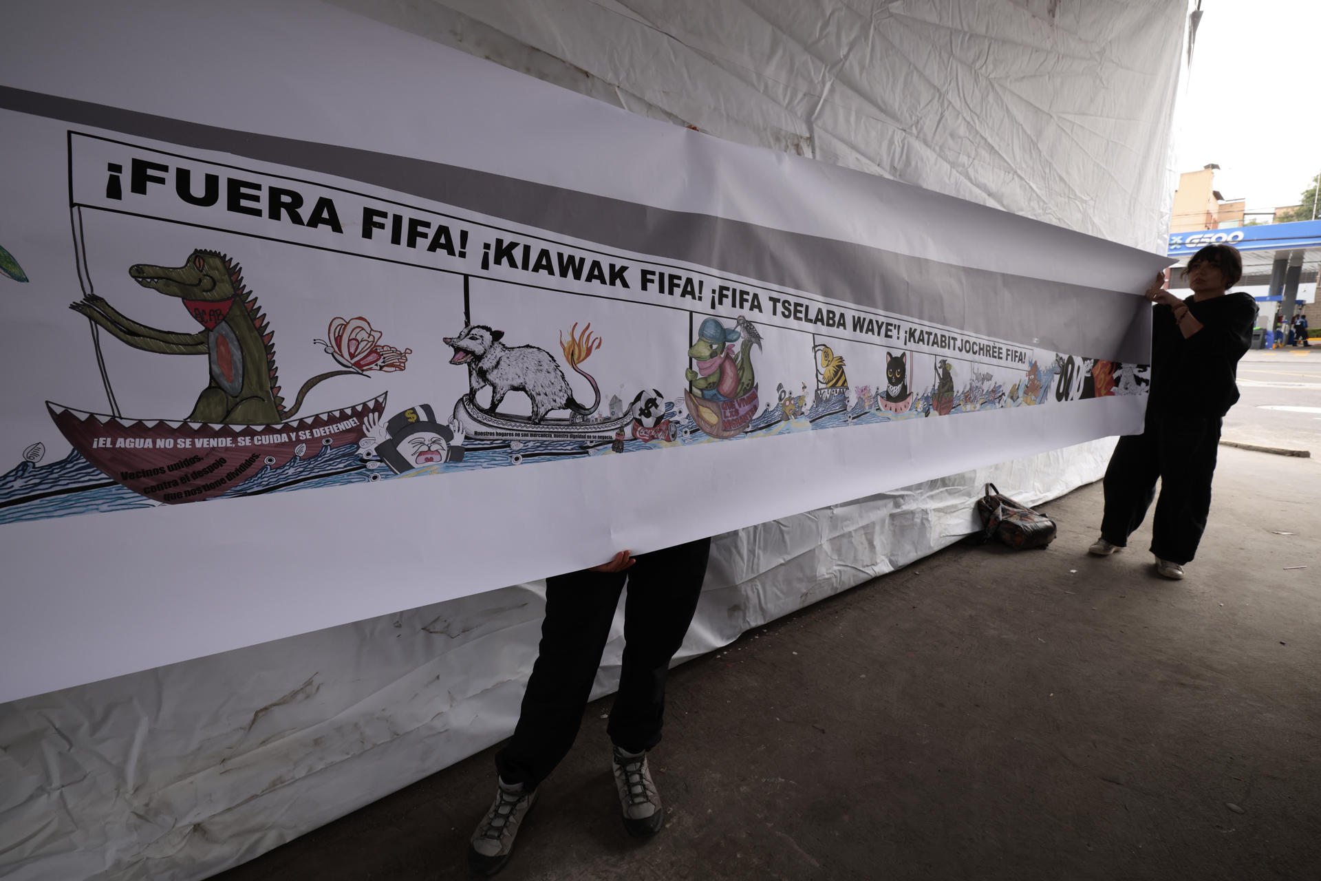 Activistas sostienen un cartel durante una manifestación, donde acusan a las autoridades de intentar "borrar" sus demandas por el acceso al agua y la defensa del territorio, tras el retiro de un mural comunitario instalado en las inmediaciones del estadio Azteca, este martes en Ciudad de México (México). EFE/ José Méndez
