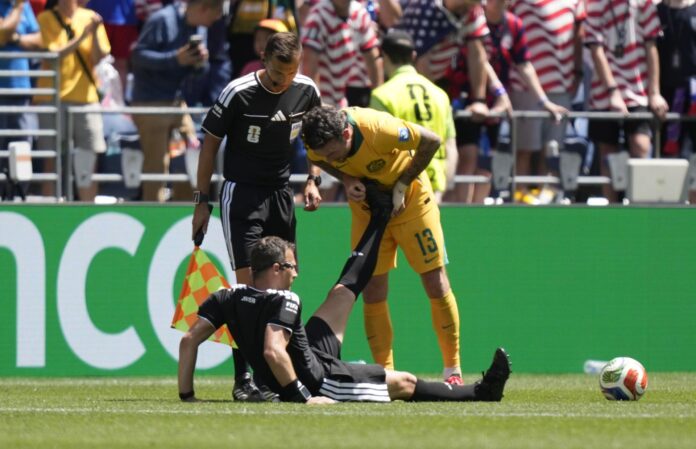 El jugador Aiden O'Neill, de Australia (d) ayuda al árbitro Felix Zwayer (abajo), quien sufrió calambres en el partido del Mundial 2026 ante Estados Unidos jugado en Seattle. EFE/EPA/STEPHAN BRASHEAR
