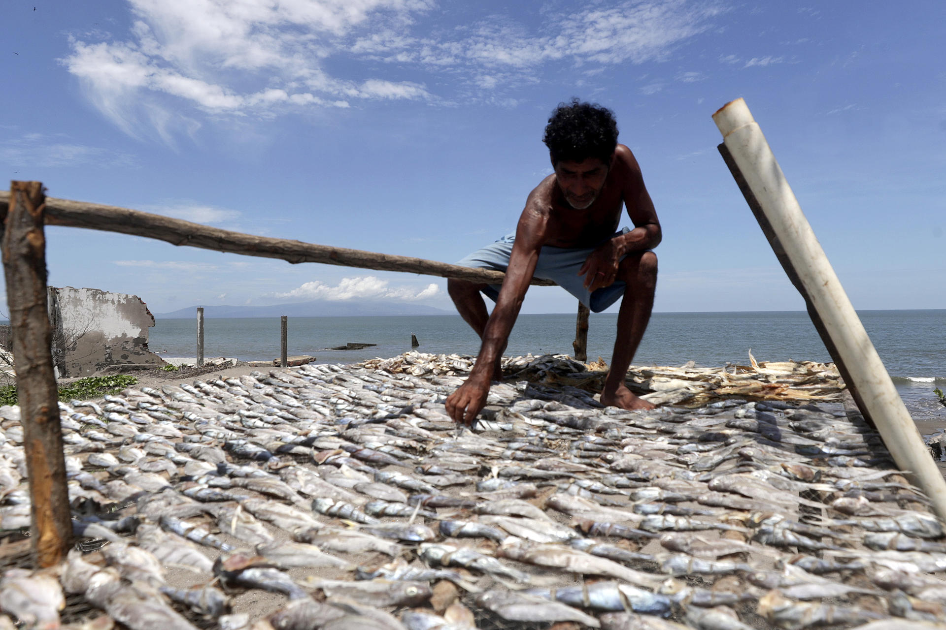 Fotografía del 18 de junio de 2026 que muestra a un hombre secando pescados sobre los escombros de una casa destruida en la aldea Cedeño, al sur de Honduras. EFE/Gustavo Amador
