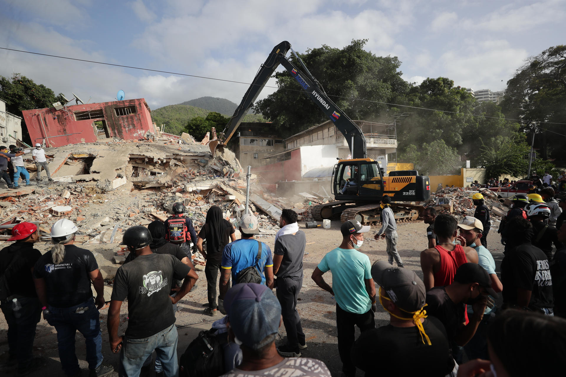 Vista general este 26 de junio de un grupo de personas al observar las labores de remoción de escombros de una retroexcavadora, dos días después del par de terremotos que azotaron el centro norte de Venezuela, en el estado La Guaira. EFE/Ronald Peña
