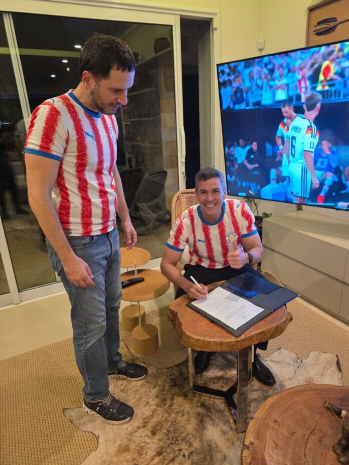 Fotografía difundida en la cuenta en X @SantiPenap del presidente de Paraguay, Santiago Peña (d), firmando el decreto N.º 6280 que declara feriado nacional el martes 30 de junio para celebrar la clasificación de la selección a los octavos de final del Mundial de la FIFA 2026 tras vencer a Alemania. EFE/ @SantiPenap /SOLO USO EDITORIAL/ SOLO DISPONIBLE PARA ILUSTRAR LA NOTICIA QUE ACOMPAÑA (CRÉDITO OBLIGATORIO)

