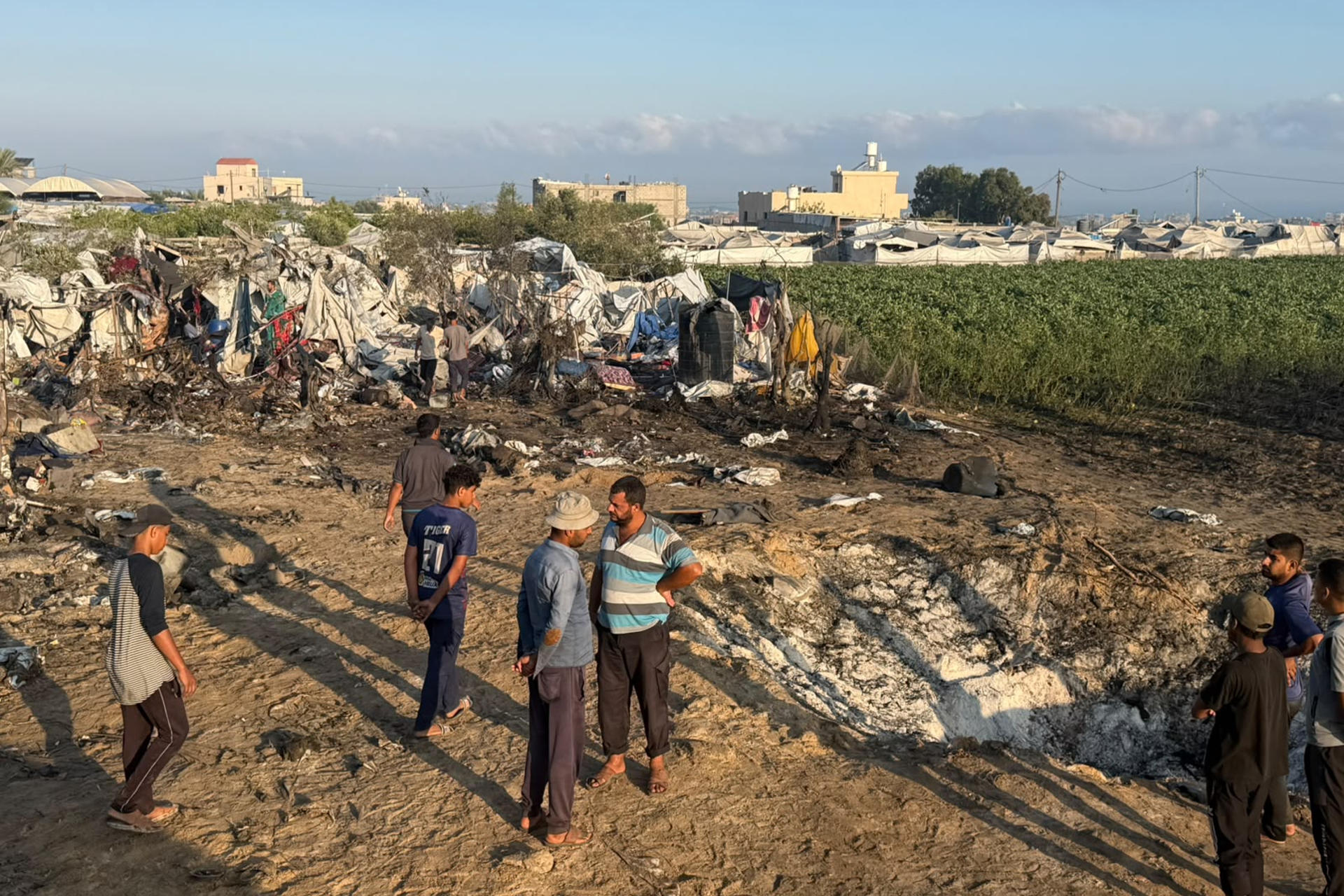 Varios hombres permanecen sobre los restos del campamento donde residen desplazados tras un bombardeo en la noche del lunes en Jan Yunis (sur de Gaza) en el que murieron una bebé de un año y a su madre y destruyó al menos un centenar de tiendas de campaña, indicó este martes el servicio de emergencias gazatí de Defensa Civil. EFE/
