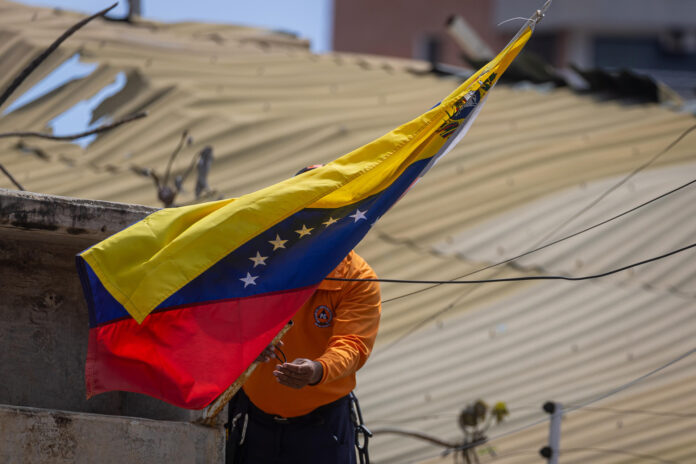 Un integrante de la Protección Civil de Venezuela coloca una bandera en una zona afectada por terremotos este martes, en La Guaira (Venezuela). EFE/ Miguel Gutiérrez
