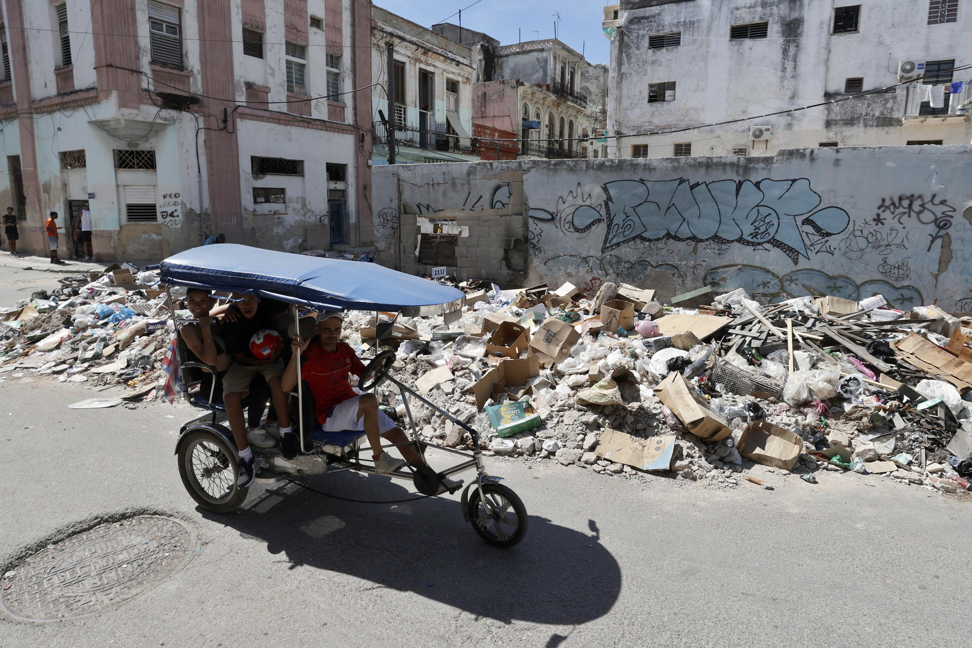 Personas se transportan en un bicitaxi junto a un basurero este jueves en La Habana (Cuba). EFE/ Ernesto Mastrascusa
