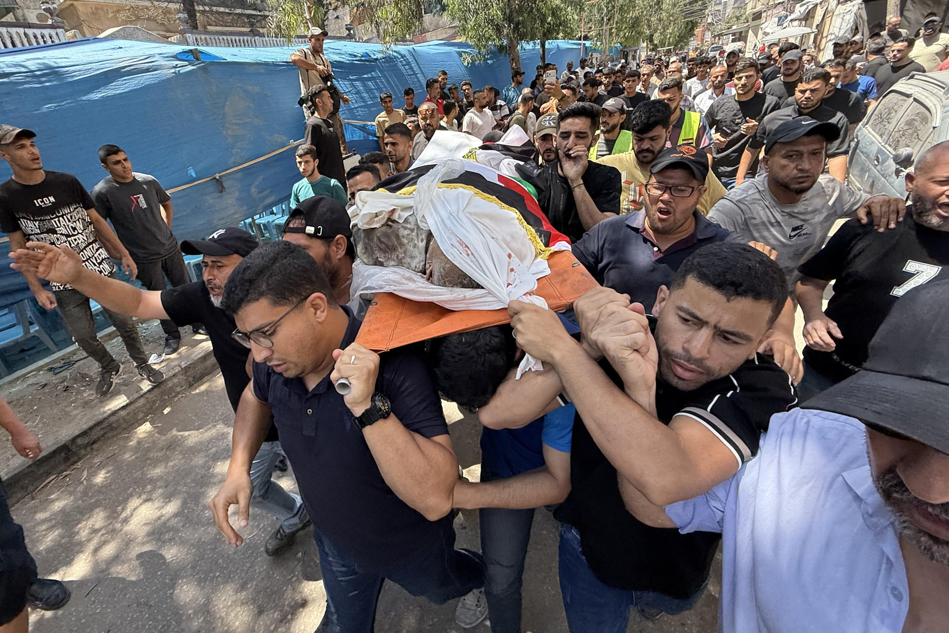 Varios hombres portan el cuerpo de Mohamed Al Wahidi, director de la Oficina de Mujtares y Notables del Comité Egipcio de Ayuda para Gaza, la agencia estatal egipcia encargada del envío de ayuda humanitaria al enclave, cubierto de una bandera egipcia, desde una ambulancia hasta su casa del barrio de Al Sabra, y de allí al cementerio, durante el funeral celebrado este miércoles en Ciudad de Gaza. El Ejército israelí mató a Al Wahidi en un ataque perpetrado en el barrio de Al Sabra de Ciudad de Gaza en el que también murieron dos niños de 8 y 10 años y un hombre de 30 años, según informó el hospital gazatí Al Shifa. El ataque coincidió con el partido Egipto - Argentina del Mundial de fútbol, que miles de gazatíes siguiendo en apoyo al país vecino. EFE/ Ahmad Awad
