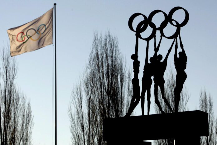 Fotografía de archivo del 12 de diciembre de 2007, en la que puede verse una bandera y una escultura con los aros olímpicos, fotografiadas frente a la sede del Comité Olímpico Internacional (COI) en Lausana, Suiza. EFE/Laurent Gillieron
