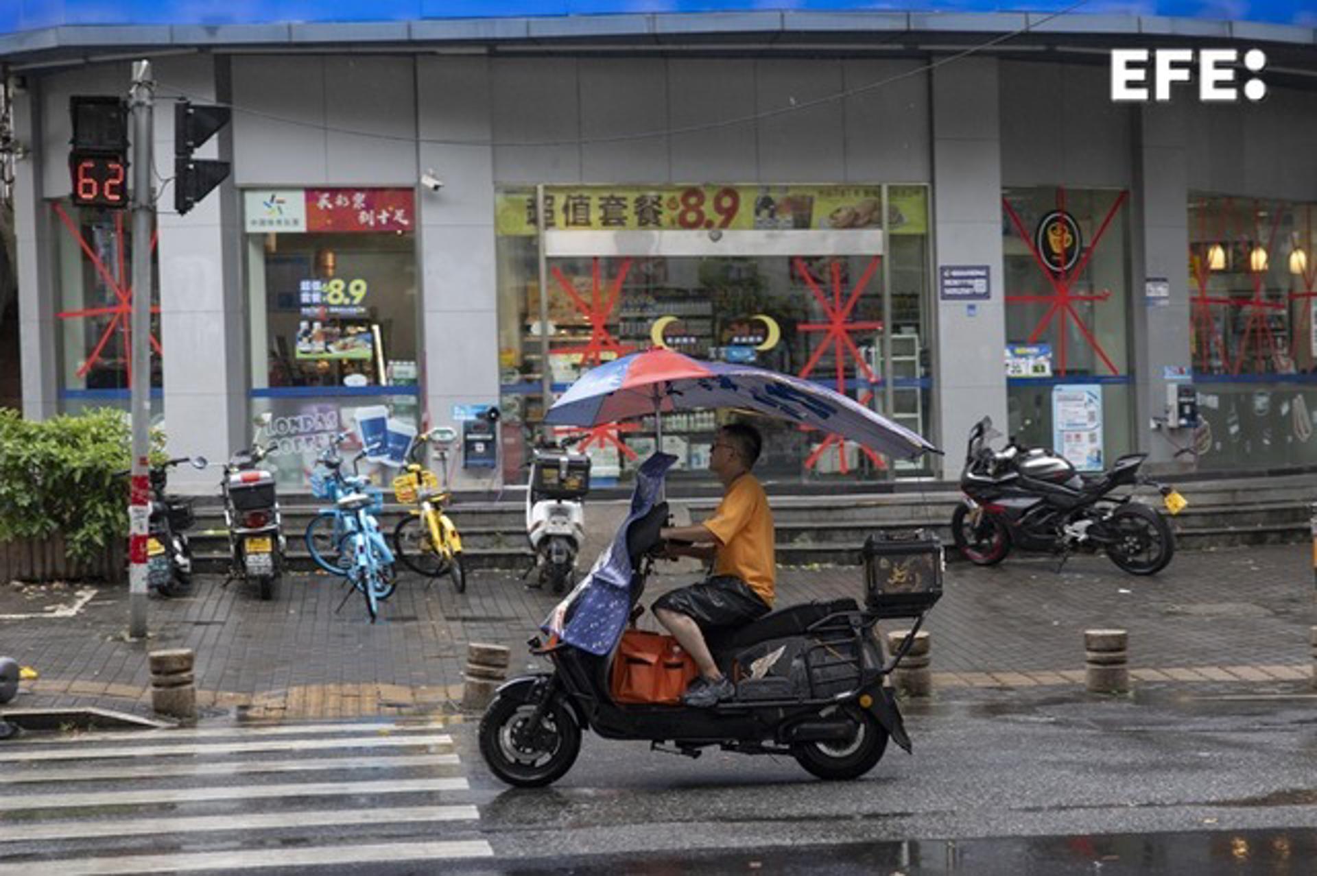 WENZHOU (China), 11/07/2026.- Un hombre conduce una moto frente a una tienda de conveniencia, cuyos escaparates están protegidos con cinta adhesiva ante la llegada del tifón Bavi, en Wenzhou (provincia de Zhejiang, China), el 11 de julio de 2026. EFE/EPA/ANDRES MARTINEZ CASARES
