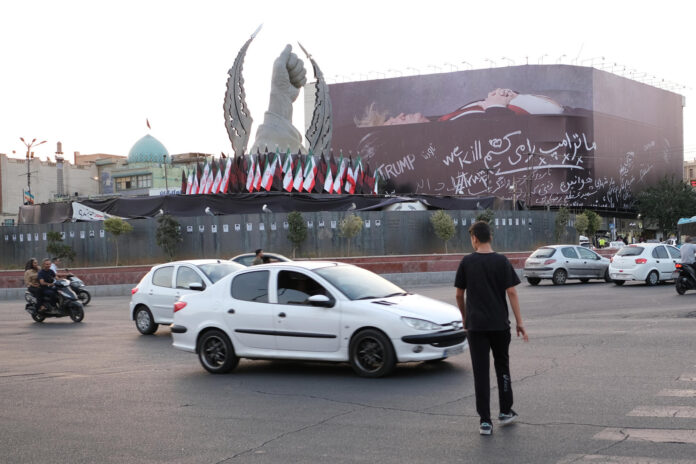 Un hombre cruza el paso peatonal a unos metros de un enorme mural que muestra al presidente estadounidense Donald Trump en un ataúd, acompañada de una frase en persa que dice: 