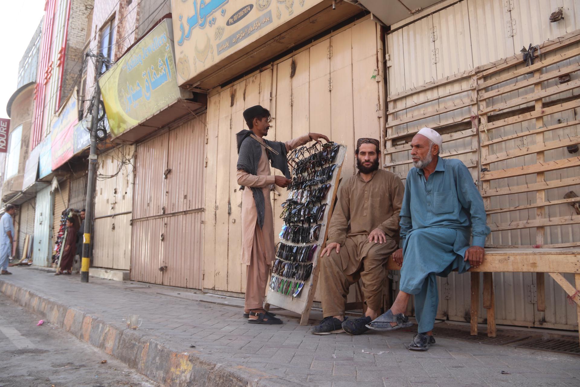 Unas personas se sientan frente a comercios cerrados durante una huelga general en Quetta, Pakistán, este viernes. EFE/EPA/FAYYAZ AHMAD
