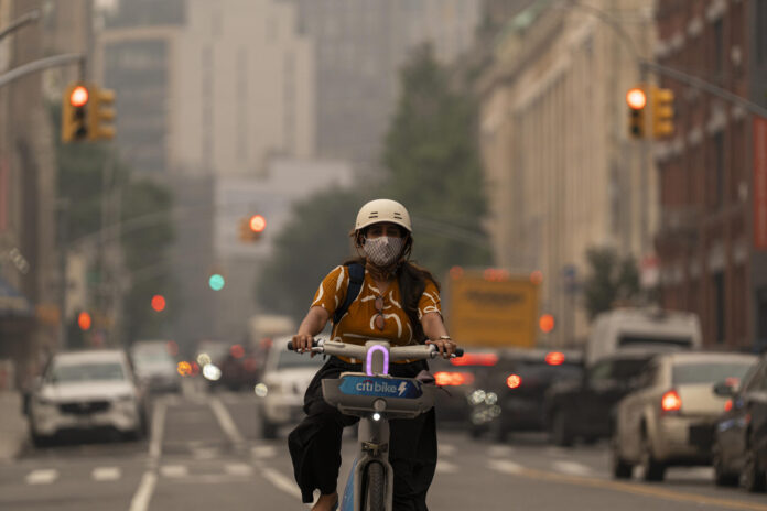 Una joven fue captada este 17 de julio al transitar en bicicleta y con tapabocas, en medio de un densa capa de humo procedente de los incendios forestales en Canadá, en Manhattan (NY, EE.UU.). EFE/Ángel Colmenares
