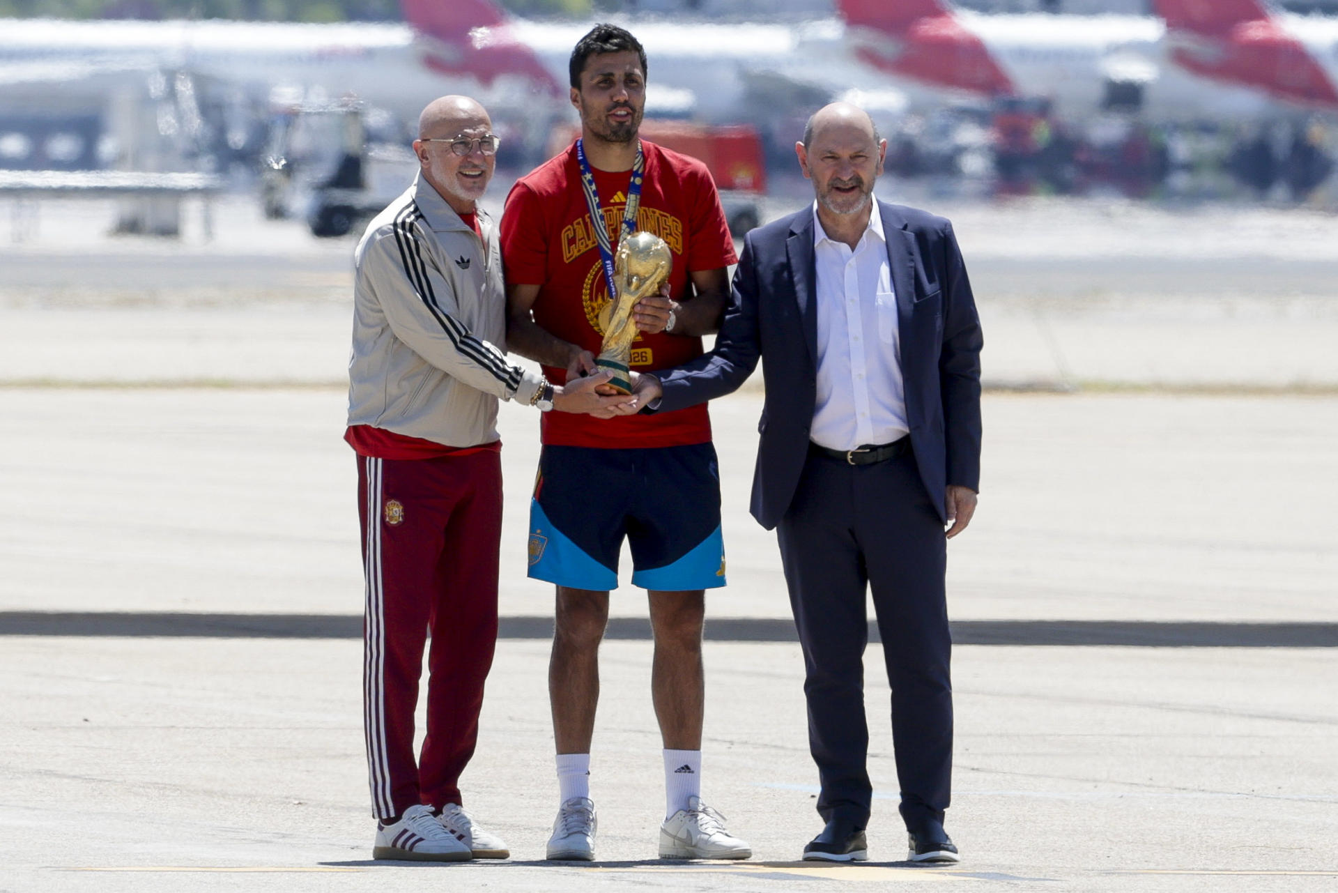 El capitán de la selección española de fútbol, Rodri (c), que lleva el trofeo de la Copa del Mundo, acompañado del seleccionador nacional, Luis de la Fuente (i), y el presidente de la RFEF, Rafael Louzán, a su llegada al aeropuerto de Madrid Barajas después de proclamarse anoche campeona del Mundial en Estados Unidos tras vencer a Argentina en la final. EFE/ J.J.Guillen