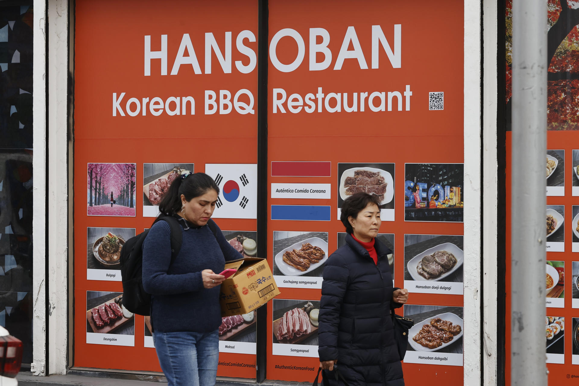 Un par de mujeres fue captado al caminar frente a un restaurante de comida coreana, en Santiago de Chile. EFE/Elvis González
