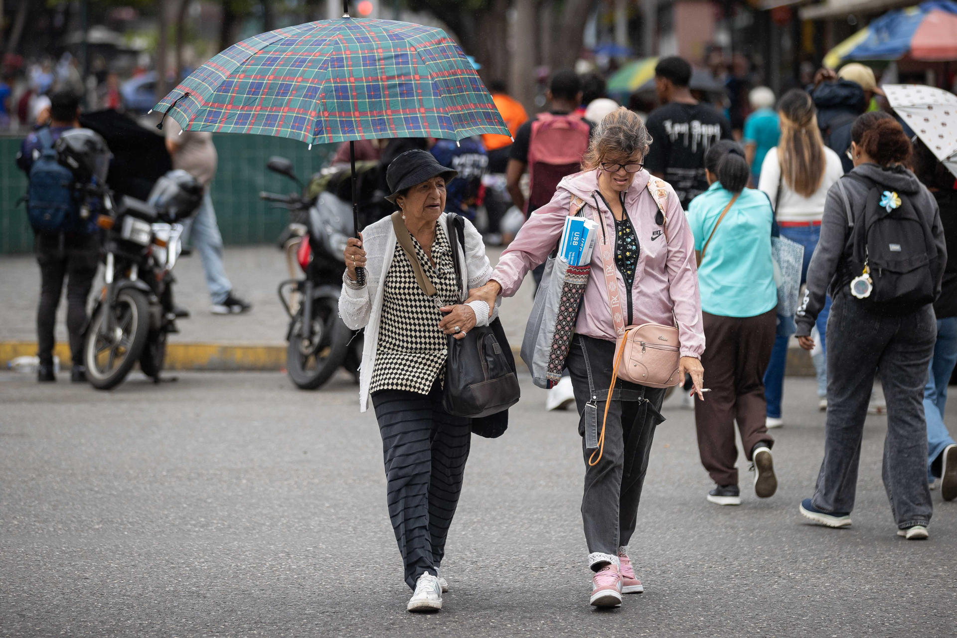 Personas se protegen de la lluvia este lunes, en Caracas (Venezuela). EFE/ Ronald Peña R