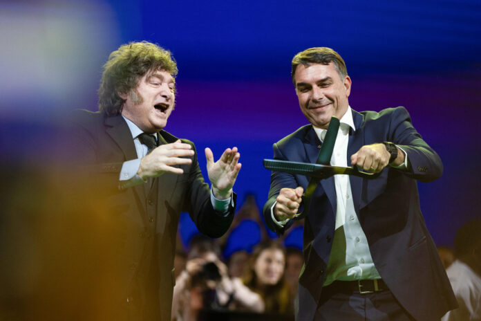 El senador de Brasil Flávio Bolsonaro (d) reacciona junto al presidente de Argentina, Javier Milei, durante la convención nacional del Partido Liberal de Brasil (PL) este sábado, en São Paulo (Brasil). El PL que lidera el expresidente Jair Bolsonaro, dio inicio a la convención para proclamar a su hijo mayor, Flávio, como candidato presidencial para las elecciones del próximo octubre. EFE/ Isaac Fontana
